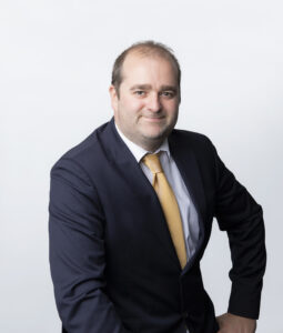 Man in blue suit, sitting down, facing camera slightly side on