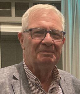 Headshot of man facing camera, he has grey hair and is wearing glasses